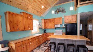Une cuisine avec des meubles de rangement en bois, un îlot central doté de tabourets, un four à micro-ondes et un réfrigérateur.
