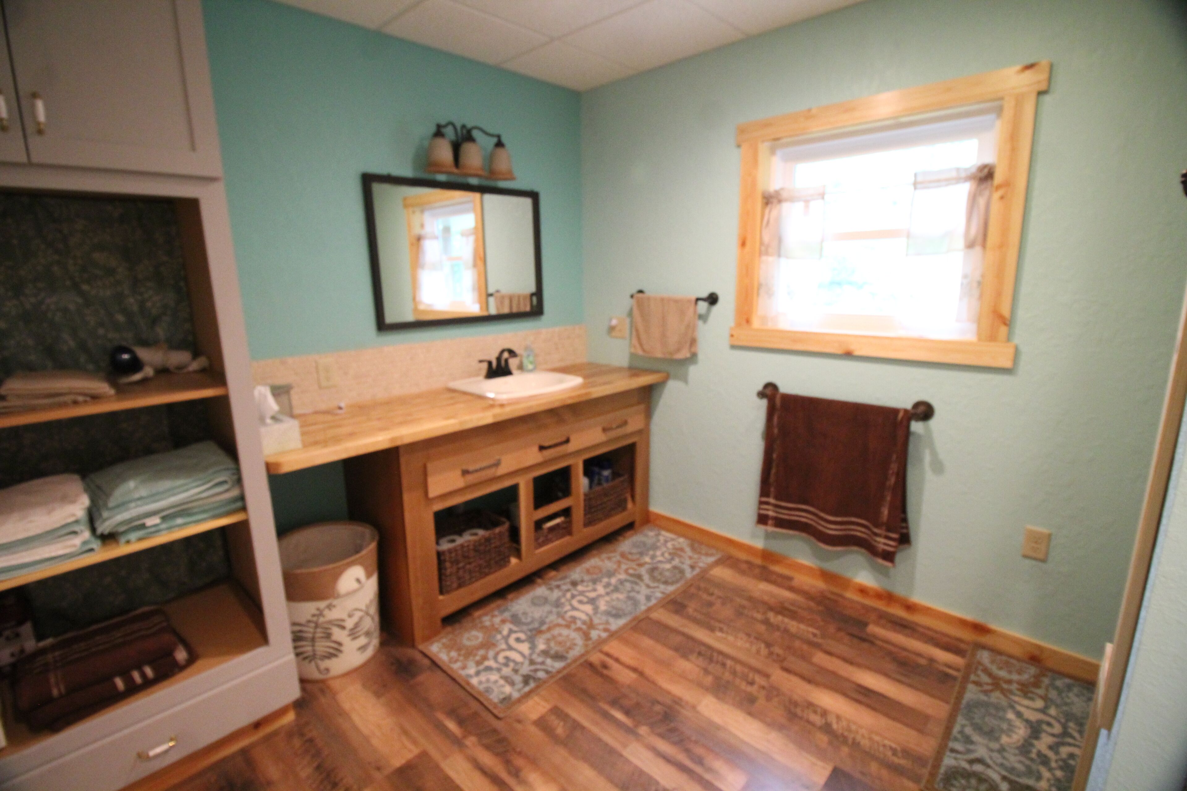 Une salle de bain avec un meuble-lavabo en bois, un évier, un miroir, une fenêtre et un porte-serviettes.