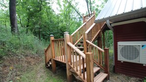 Un escalier en bois mène à une cabane surmontée d’un toit en métal, elle-même entourée d’une forêt dense.