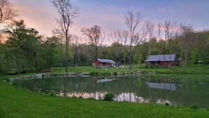 Une propriété paisible située au bord d’un lac, avec deux granges rouges, un étang et une végétation luxuriante tout autour.