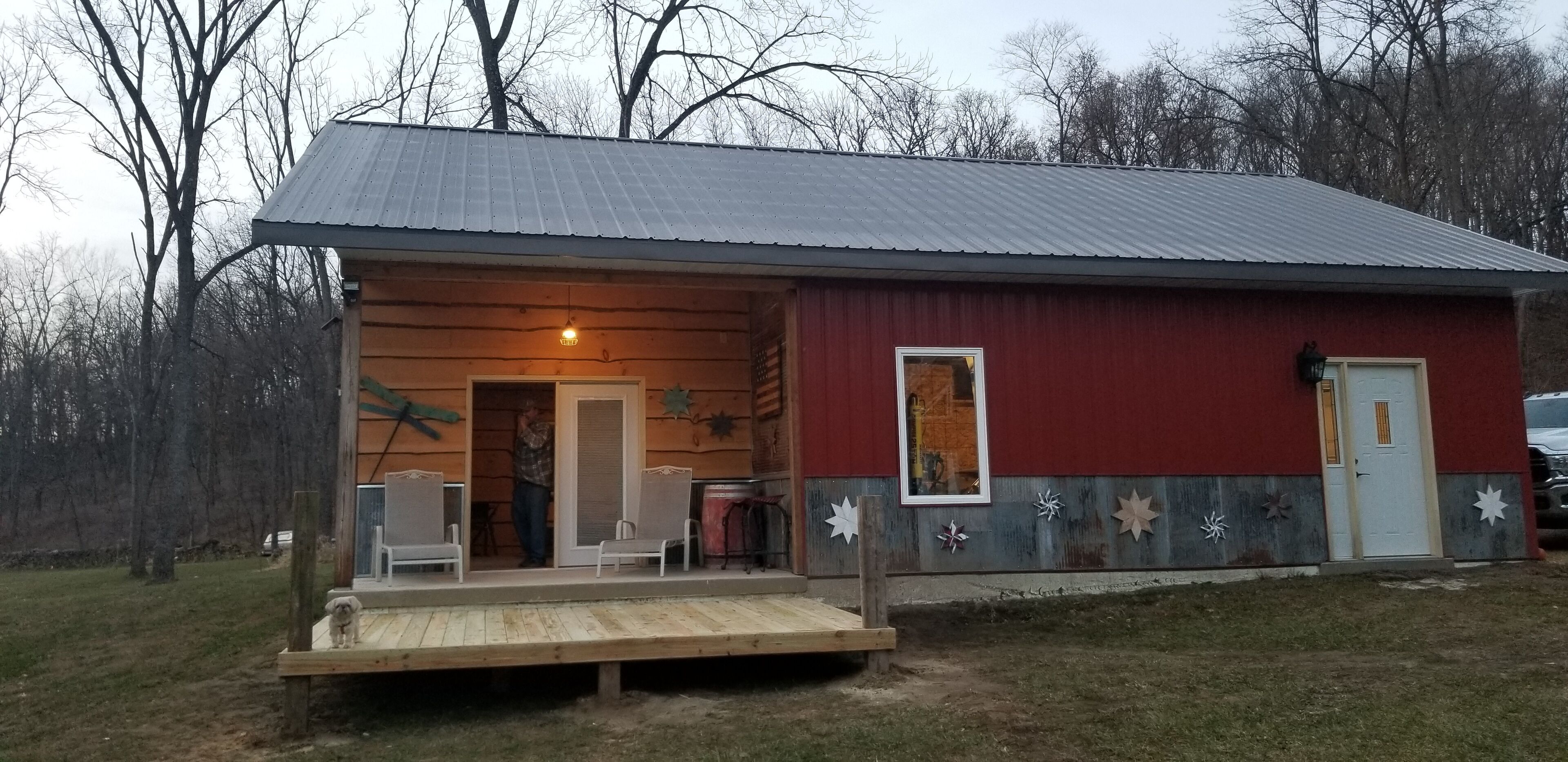 Une cabane en bois avec un toit en métal, une véranda avec des chaises et une petite terrasse.