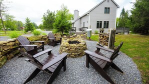 Une maison avec un foyer en pierre et des fauteuils Adirondack en bois dans la cour.