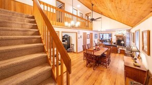 Un vaste espace de vie aménagé dans un style industriel, avec un escalier en bois, une table à manger et une cheminée.