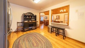 Une cuisine avec un plancher en bois, un réfrigérateur, un meuble sombre en bois, un tapis et un banc.