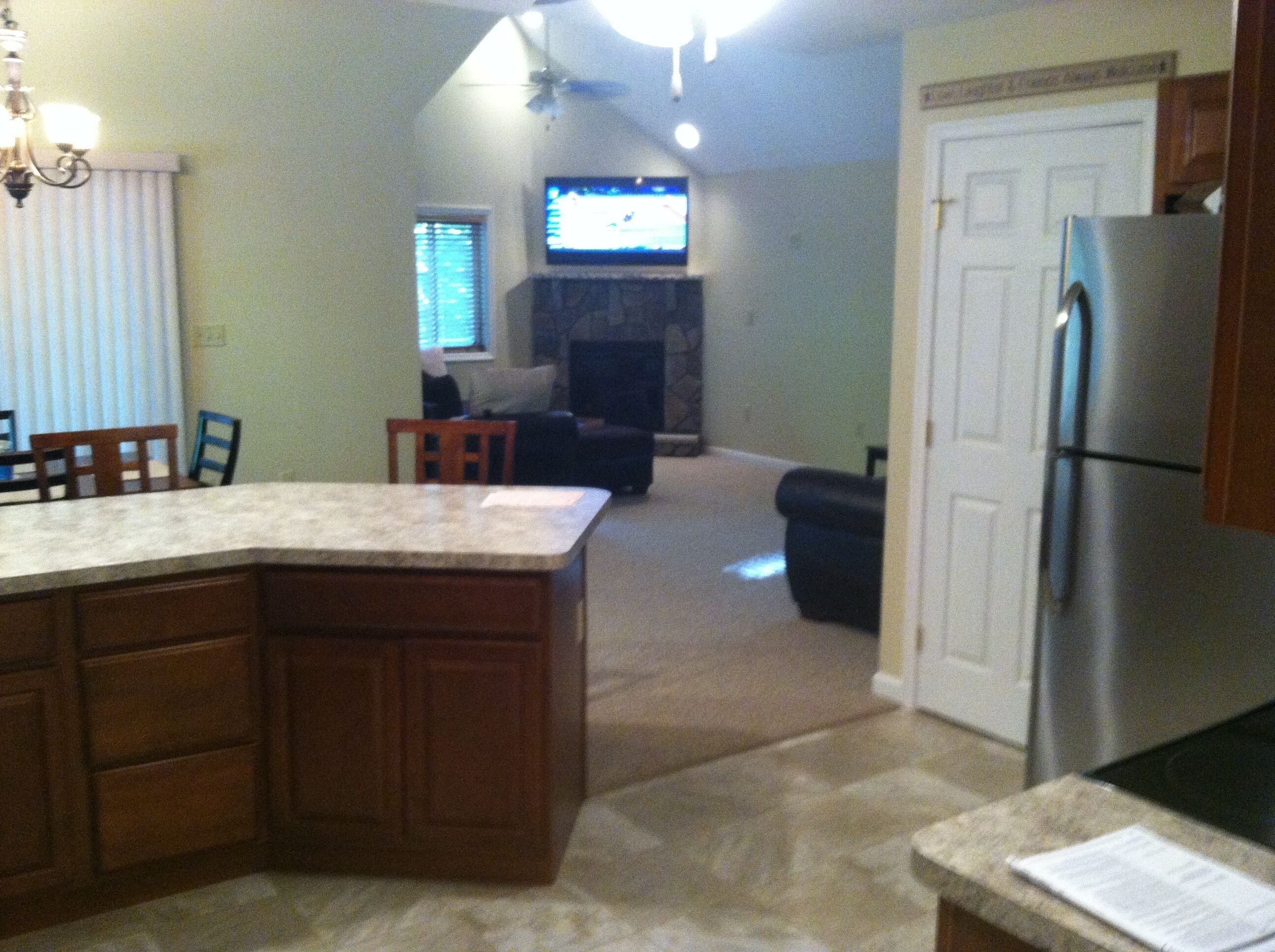 A kitchen with a central island, a dining area with a table and chairs, a living room with a couch and a TV, and a refrigerator.