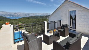 En balkon med fletmøbler, en pool og en smuk udsigt over bjerge og vand.