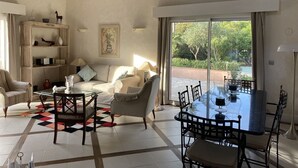 A living room with a sofa, armchairs, a coffee table, and a dining table with chairs. There is a bookshelf and a painting on the wall. - Saint Raphael beautiful villa 170 m2 swimming pool, very quiet, comfortable, residential  (Saint-Raphaël)