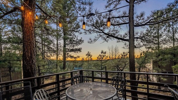 A deck with metal chairs and a table, surrounded by trees and string lights. - HIDDEN VISTA: Distance views from private oversized deck nestled in cool pines. (Munds Park)