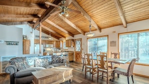 A spacious living room with a wooden ceiling, a dining area with wooden chairs, and a kitchen in the background. - HIDDEN VISTA: Distance views from private oversized deck nestled in cool pines. (Munds Park)