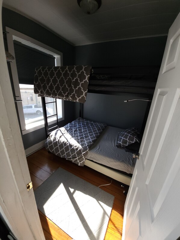 A compact room with a bunk bed, a window with blinds, a door, and a small rug on the floor. - Fulton market / Noble Square FREE parking, Laundry, 2.5 miles to Mag Mile! (Chicago)