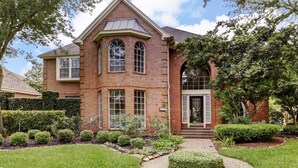 A two-story brick house with a symmetrical facade, large windows, and a well-maintained garden with a circular hedge and trimmed bushes. - Luxury Spectacular House in TX (Sugar Land)