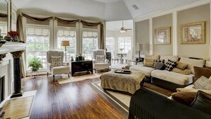 A spacious living room with a fireplace, large windows, and a ceiling fan. - Luxury Spectacular House in TX (Sugar Land)