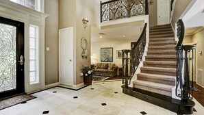 A spacious foyer with a grand staircase, a large mirror, and a floral arrangement. - Luxury Spectacular House in TX (Sugar Land)