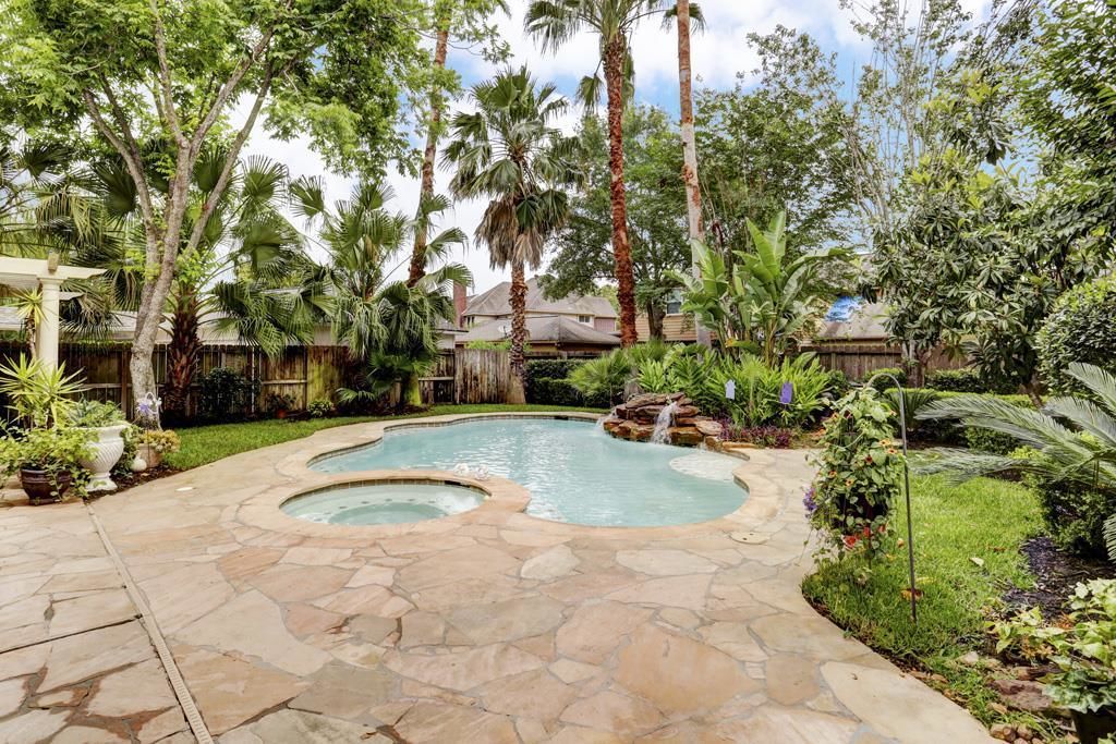 A backyard with a stone pool, palm trees, and a waterfall feature.