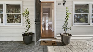 Entrada d'una casa amb una porta de fusta, plantes en testos i un felpó.