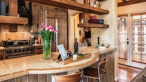 Une cuisine avec des meubles de rangement en bois, un îlot central doté de tabourets, un vase rempli de fleurs roses et un ensemble de verres à vin.