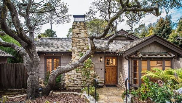Une maison avec une cheminée en pierre, des portes en bois et un chemin en pierre menant à l’entrée.