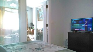 Ein Schlafzimmer mit einem Bett, einem Fernseher auf einer Kommode und einer Tür, die auf einen Balkon führt.