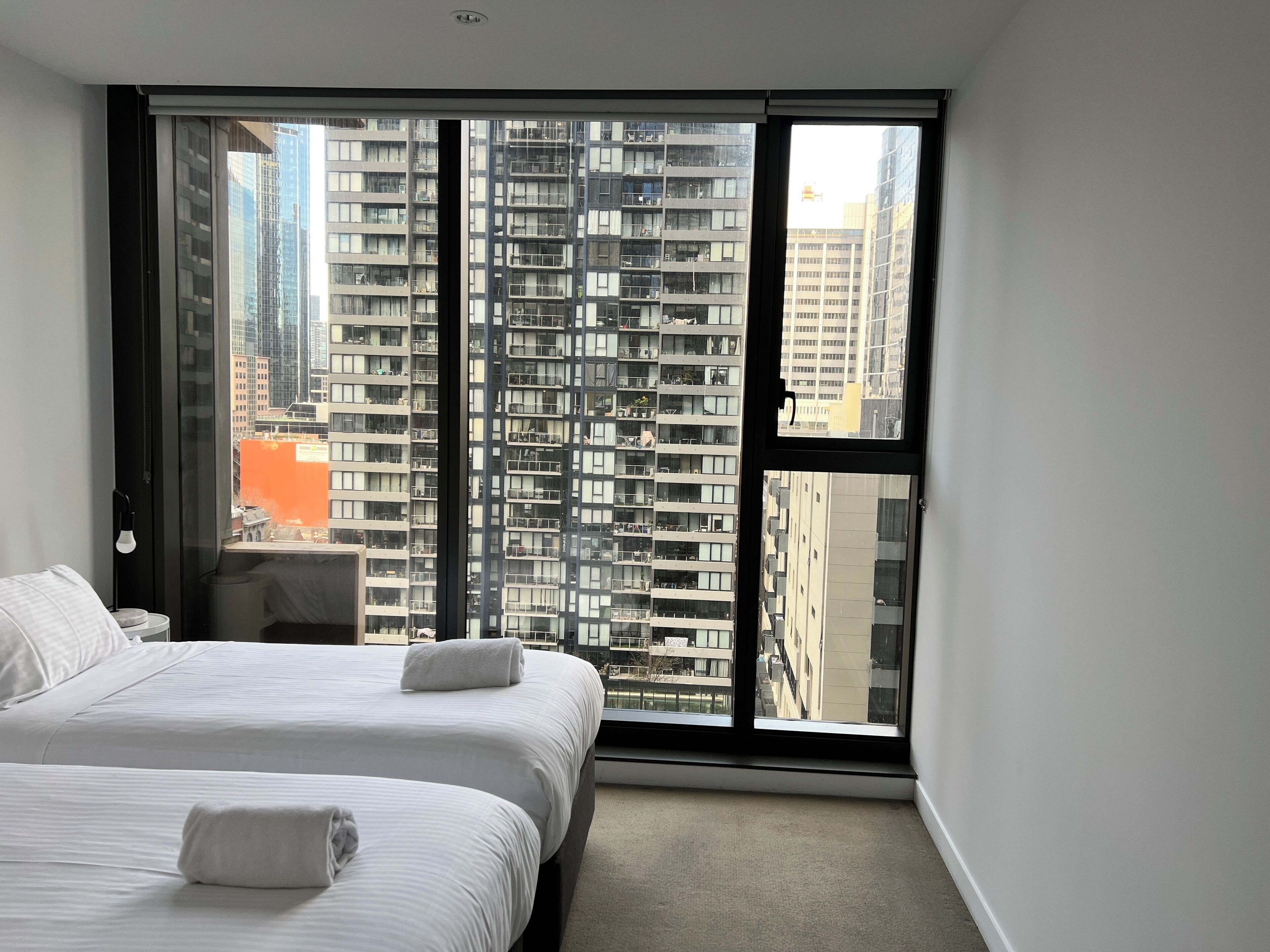 A hotel room with two beds, a large window, and a view of high-rise buildings.