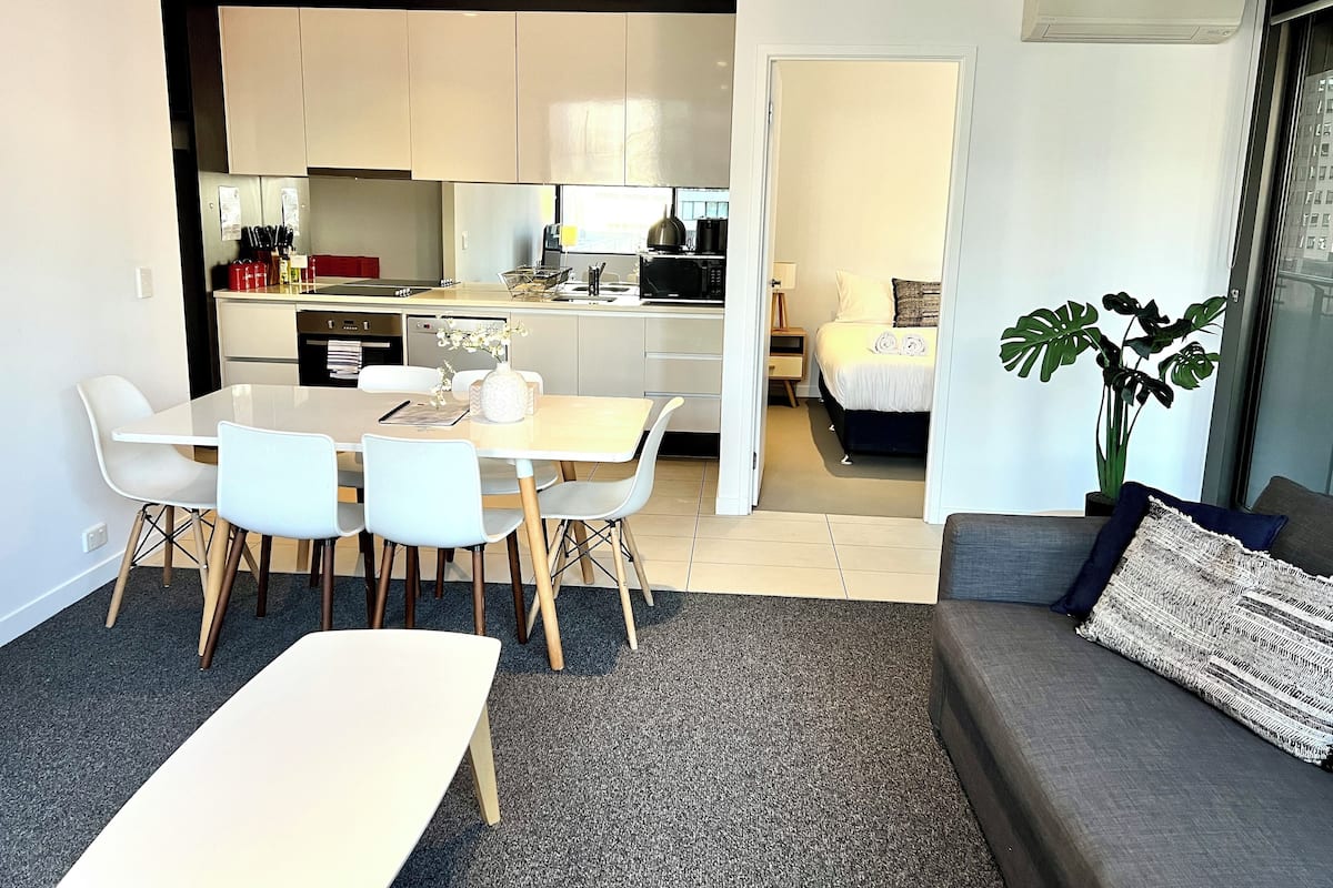 A modern apartment with a dining area, kitchenette, and a bedroom.