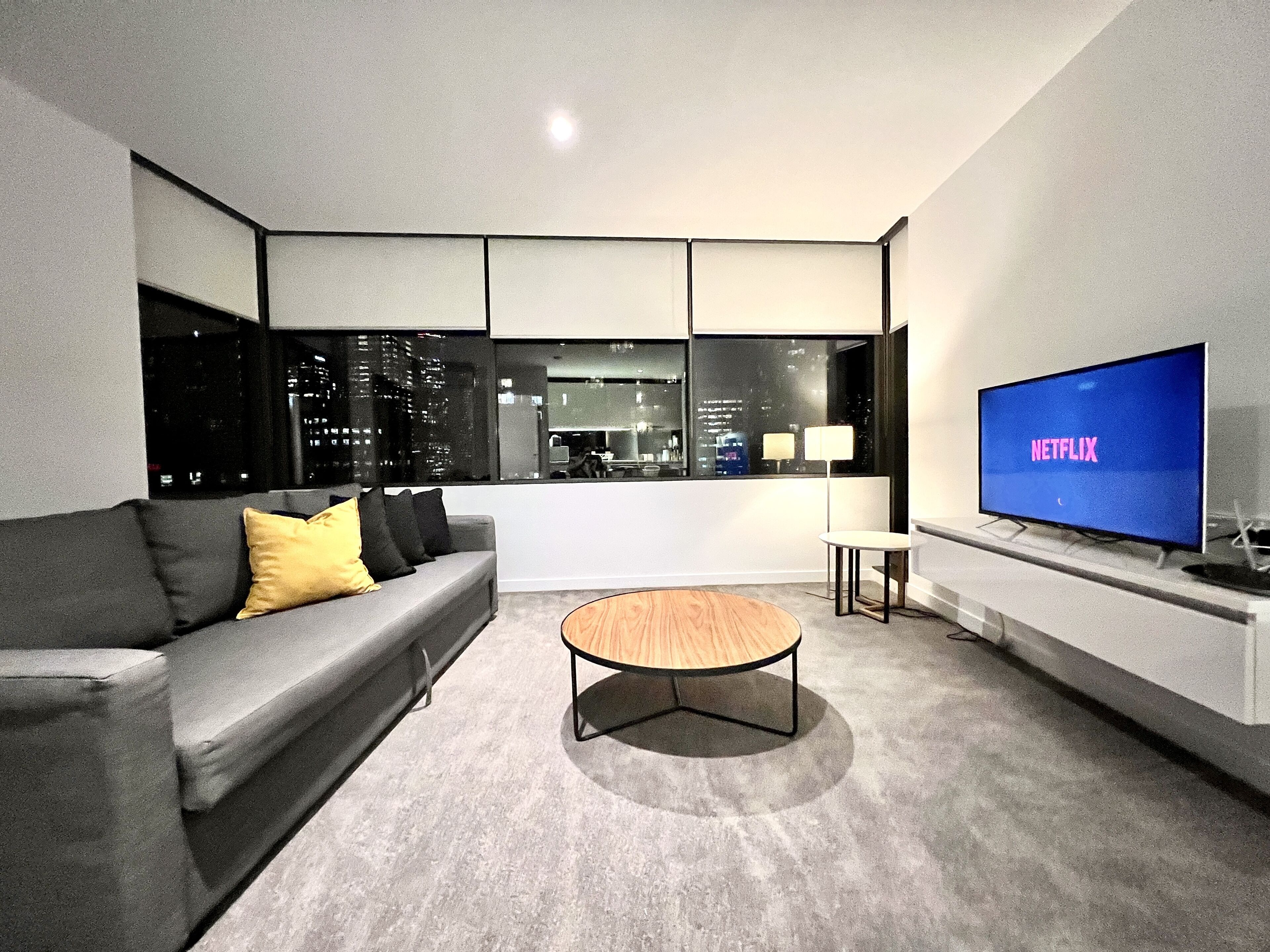 A modern living room with a grey sofa, a wooden coffee table, and a large TV displaying 'NETFLIX'.