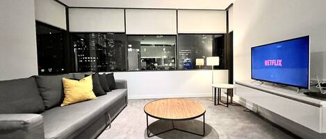 A modern living room with a grey sofa, a wooden coffee table, and a large TV displaying 'NETFLIX'.