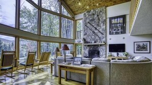 Ein geräumiges Wohnzimmer mit großen Fenstern, einem Kamin aus Stein und einer gemütlichen Sitzecke.