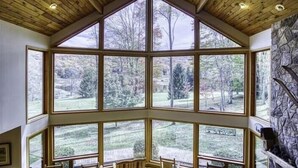 Ein Zimmer mit hohen Decken und großen Fenstern, das einen Blick auf ein bewaldetes Gebiet bietet.