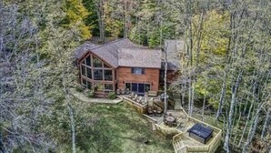 Eine Holzhütte, umgeben von dichtem Wald, mit einer großen Terrasse und einem Bereich für ein Feuerkorb.