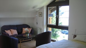 A modern room with a bed, a sofa, and two armchairs. There is a window with a view of the outside. - Maisonette apartment with mountain panorama for up to 5 people, 65 sqm, 1 bedroom (Bayerisch Gmain)