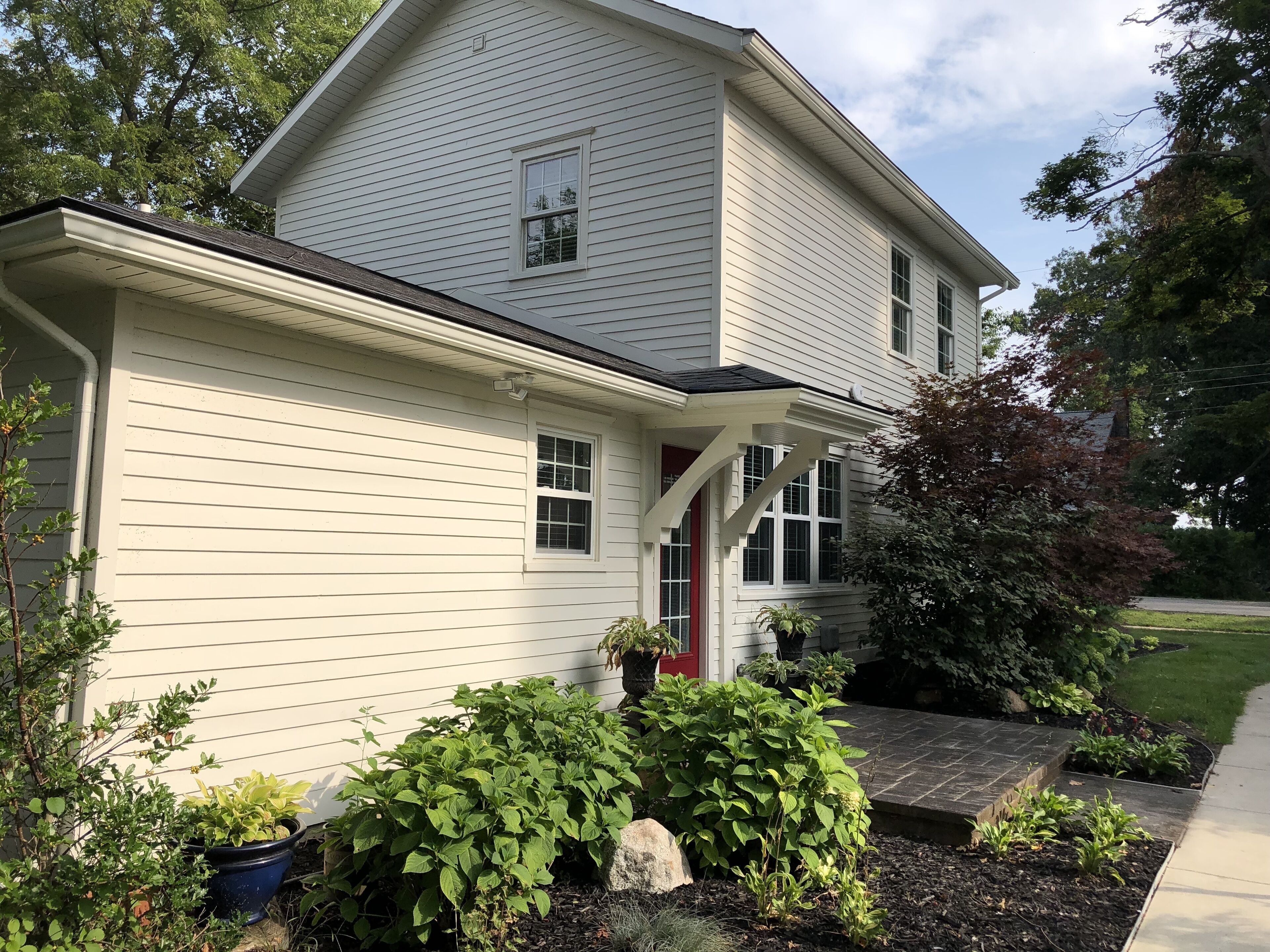 A two-story house with a white exterior, a red door, and a small porch.