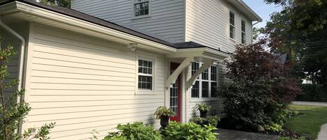 A two-story house with a white exterior, a red door, and a small porch.