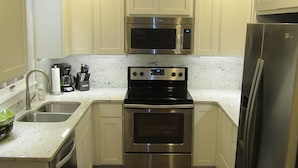 Cocina compacta con armarios blancos, refrigerador de acero inoxidable, microondas, estufa y pileta.
