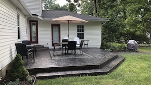 Un patio con una mesa y sillas, una sombrilla y una parrilla en el jardín.