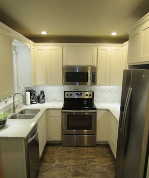 A compact kitchen with white cabinets, a stainless steel refrigerator, a microwave, a stove, and a sink. - Renovated Historic Home! 2 blocks to downtown! (Saugatuck)
