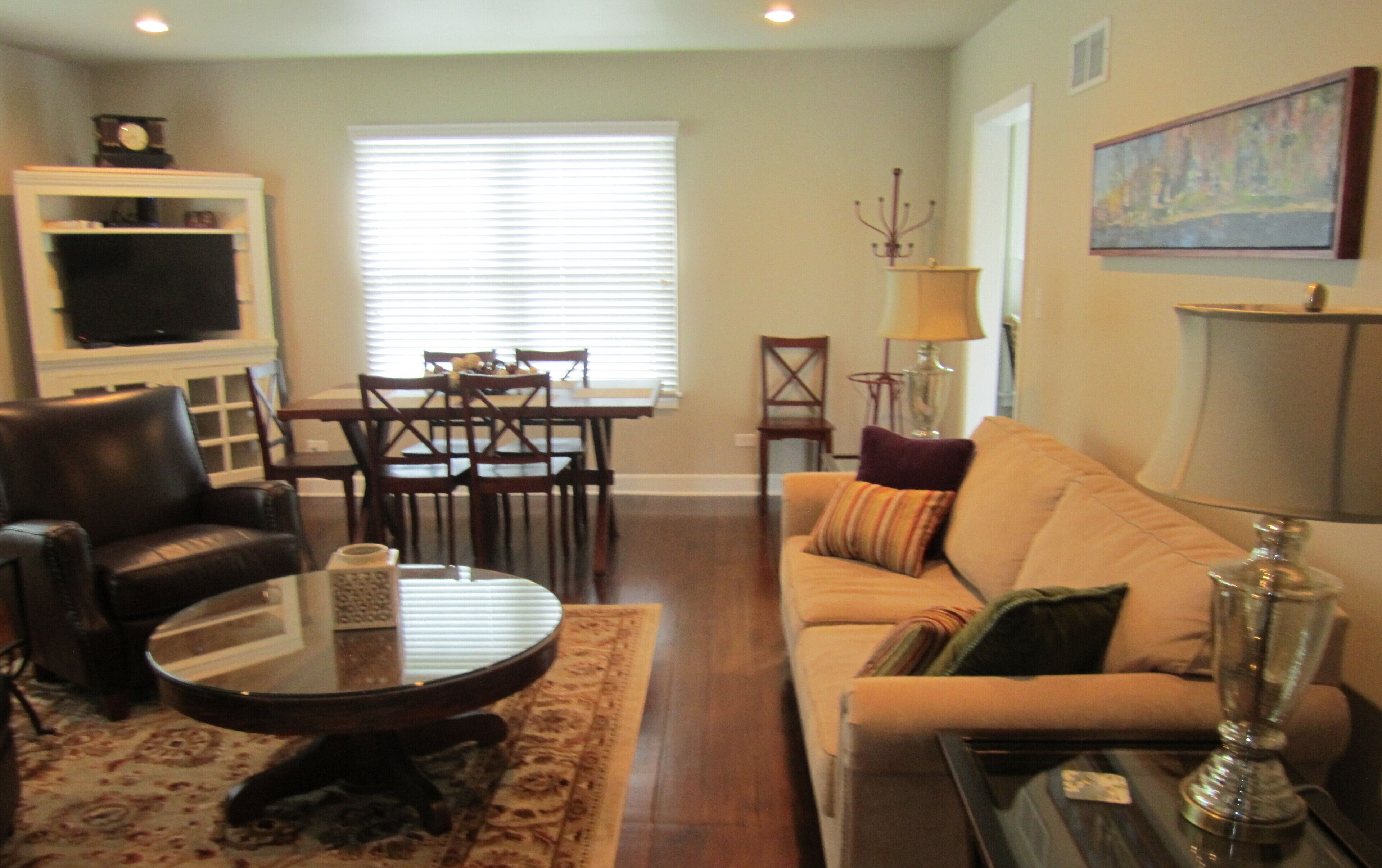 A living room with a sofa, a coffee table, a TV, a dining table with chairs, and a lamp.
