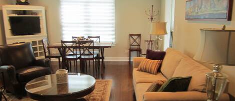 A living room with a sofa, a coffee table, a TV, a dining table with chairs, and a lamp.