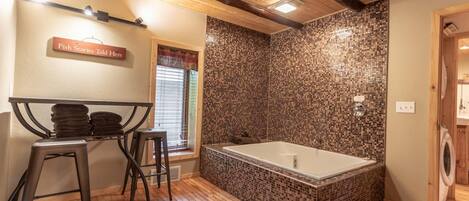 A bathroom with a mosaic-tiled wall, a wooden floor, a bathtub, and a sign that reads 'Fish Stories Told Here'.