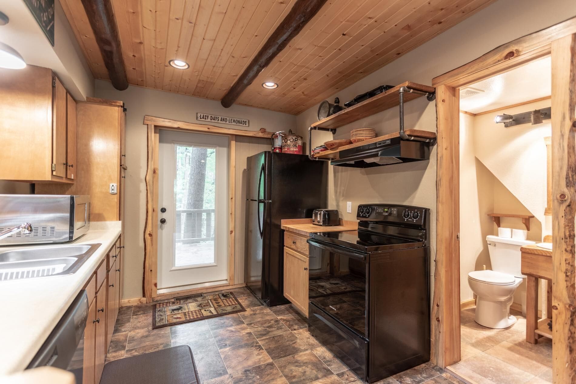 A compact kitchen with a refrigerator, stove, and sink. There's a wooden door with a window, and a shelf above the stove.