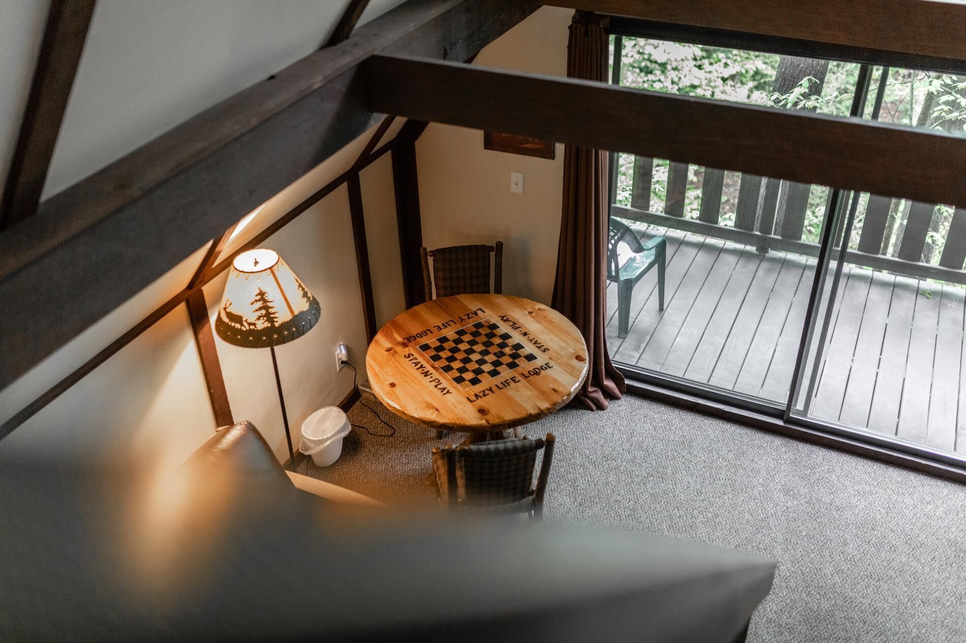 Ein gemütliches Zimmer mit einem Holztisch, der ein Schachbrettmuster zeigt, einer Lampe und Blick auf eine Holzterrasse.