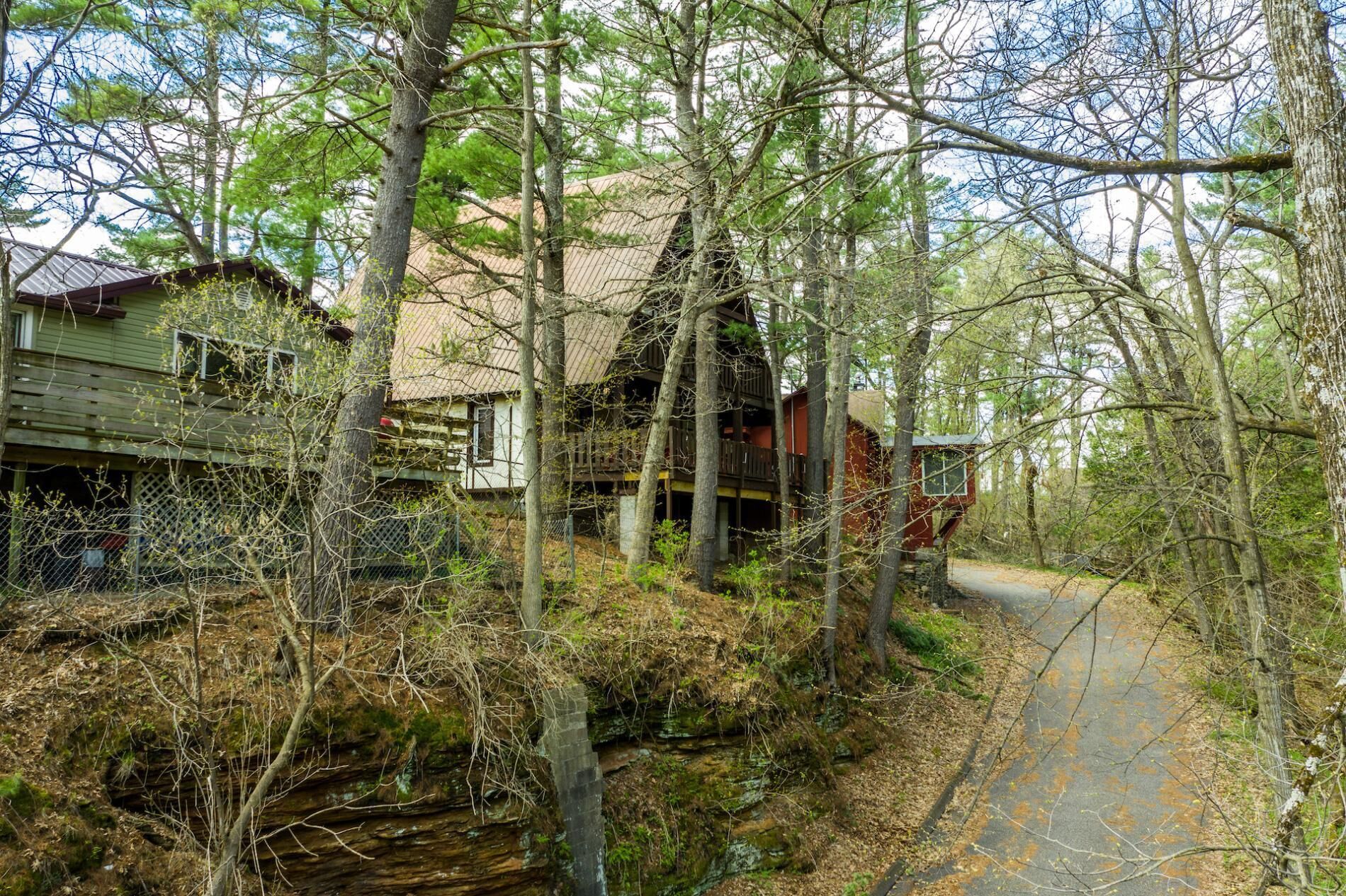 A rustic cabin with a wooden deck, surrounded by dense forest.