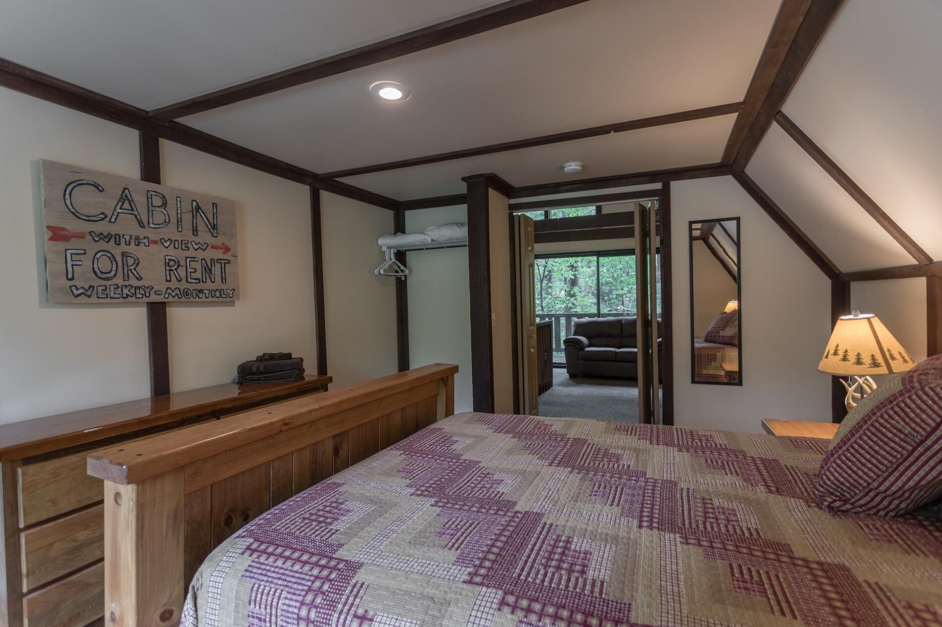 Une cabane avec un lit, un banc en bois, une pancarte au mur et une vue sur l’extérieur.