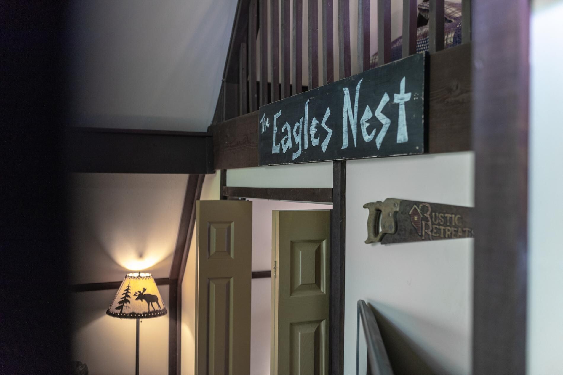 A sign reading "Eagles Nest" above a door, with a lamp displaying a moose silhouette and a rustic retreat sign on the wall.