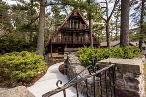 A cabin with a stone pathway leading to the entrance, surrounded by dense greenery and trees.