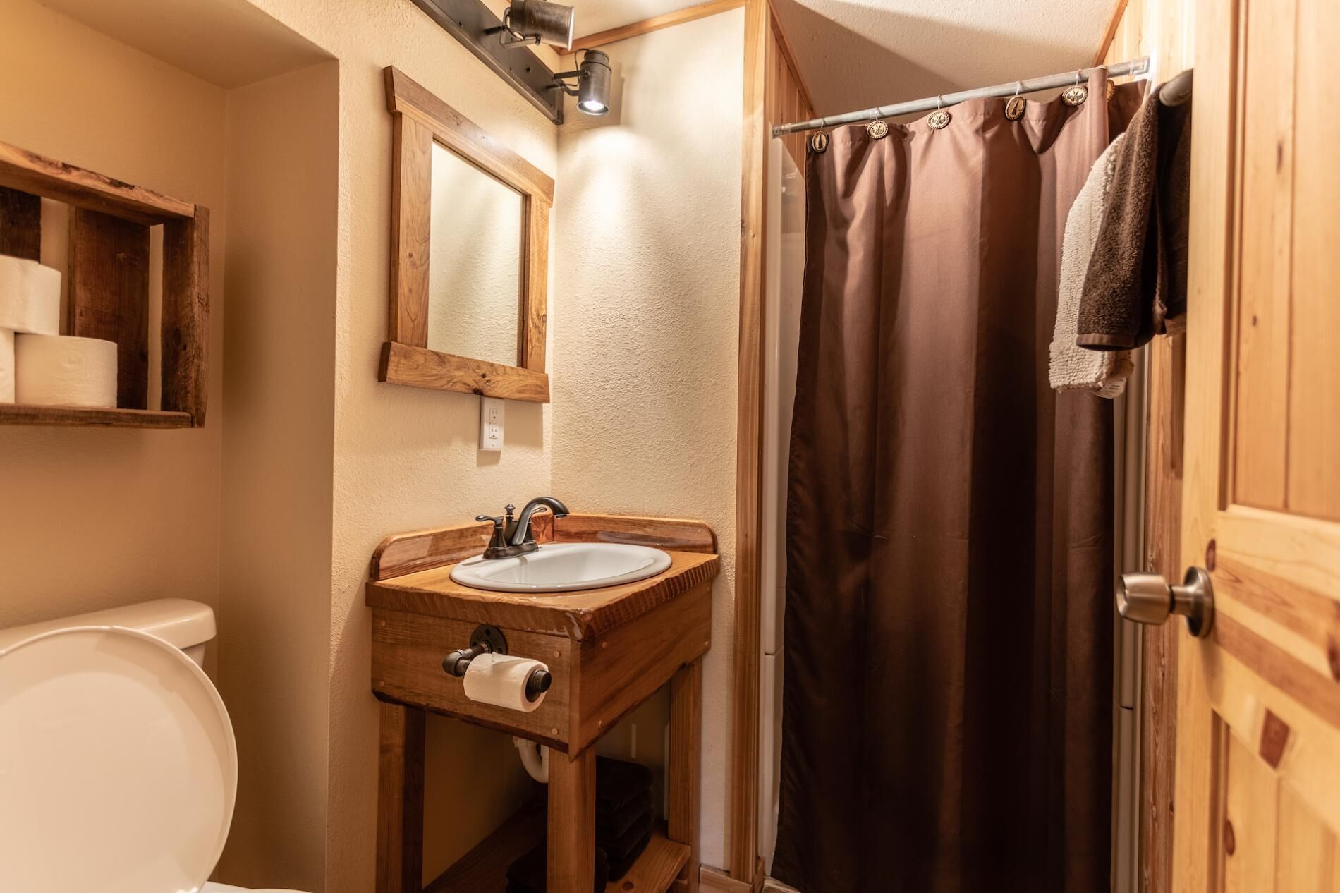 A bathroom with a wooden vanity, a white sink, a mirror, and a shower curtain.