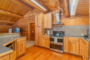 Cocina de cabaña de madera con armarios de madera, estufa de acero inoxidable y protector contra salpicaduras de piedra.