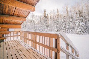 Eine Holzterrasse mit Geländer, mit Blick auf einen verschneiten Wald.