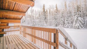 Une terrasse en bois avec une balustrade donnant sur une forêt enneigée.