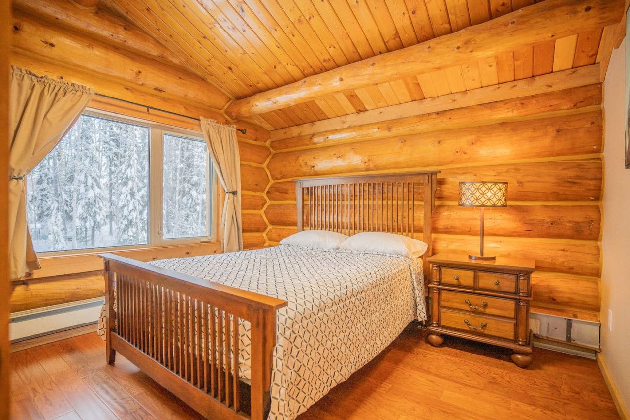 A log cabin bedroom with a wooden bed, a nightstand, and a window with curtains.