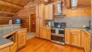Une cuisine rustique, aménagée dans une cabane en rondins, avec des meubles en bois, une cuisinière en acier inoxydable et un dosseret en pierre.